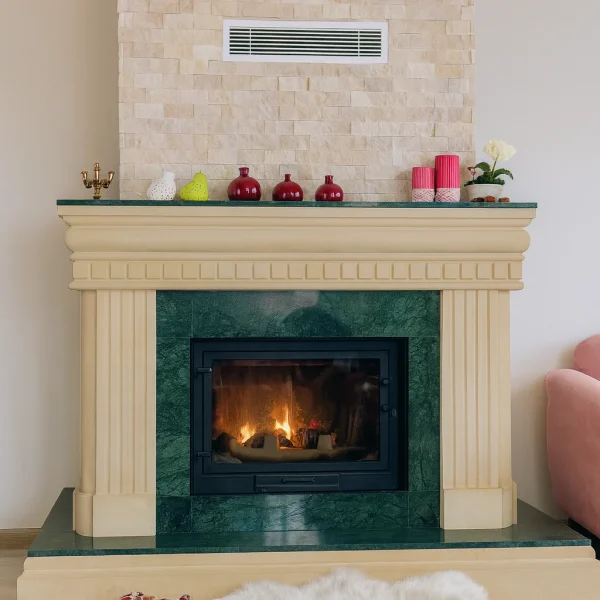 Klasik krem çerçeveli, yeşil doğal mermer yüzeye sahip odunlu şömine – oturma odasında yanan alevle sıcak atmosfer oluşturan doğal mermer detaylı şömine.