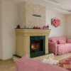 Pembe koltuklarla döşenmiş modern klasik salonda yer alan doğal mermer detaylı odunlu şömine – krem ve yeşil tonların uyumuyla öne çıkan zarif şömine modeli.