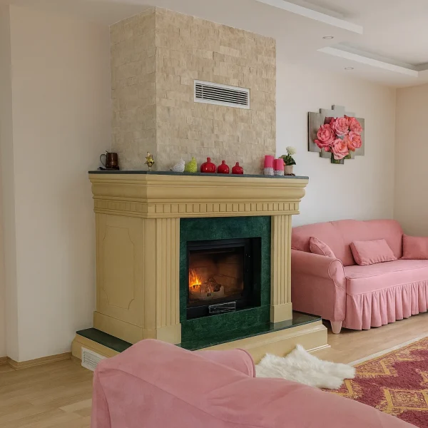 Pembe koltuklarla döşenmiş modern klasik salonda yer alan doğal mermer detaylı odunlu şömine – krem ve yeşil tonların uyumuyla öne çıkan zarif şömine modeli.